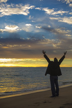 man standing in worship on a beach 