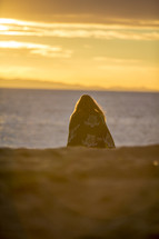 woman sitting on a beach at sunset
