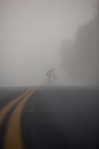 man riding a bike across the street under thick fog