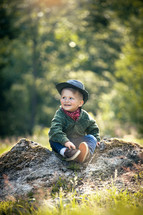 Cute Little Boy with Hat and Checkered Shirt Sitting in Summer Forest