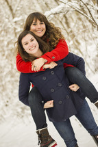 One girl holding another girl on her back, out in the snow