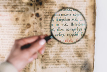 Woman researcher explores antique book with magnifier. Scientific translation of literature. Investigating manuscript with ancient writings