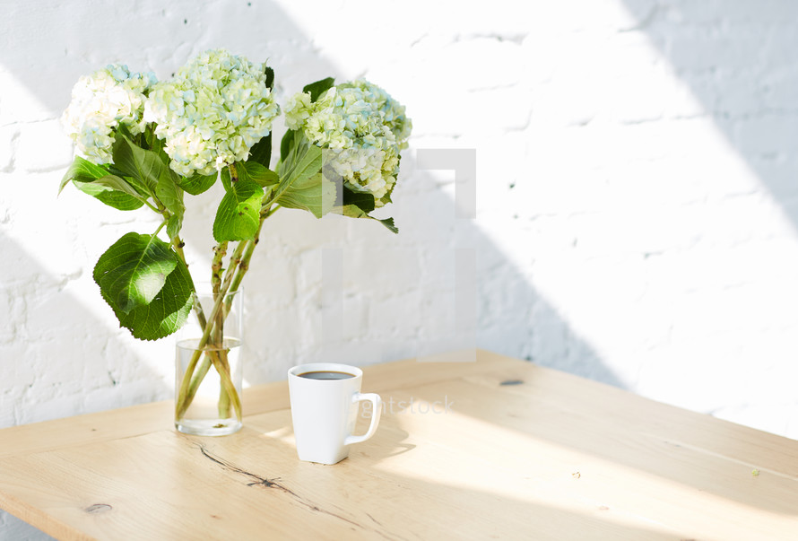 hydrangeas in a vase and coffee cup on a table 
