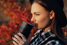 Hipster woman enjoys aroma and taste of fresh coffee. Drinking from thermos in autumn forest. Enjoy nature, holidays on mountains. High quality