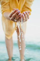 Water pouring from womans hands. Sea, close of female arms. Yellow shirt on background. Water is a life-giving force. High quality photo
