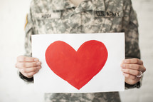 Red heart on a white sheet of paper being held by an army soldier.
