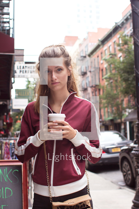 woman standing on a sidewalk holding a paper coffee cup 