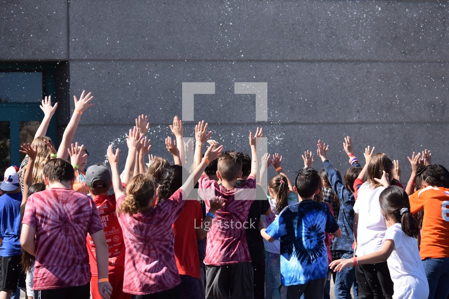 group of children with hands raised being splashed with water 