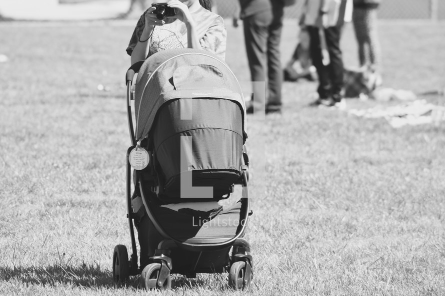 a mother pushing a stroller in the grass and taking a picture with a camera 