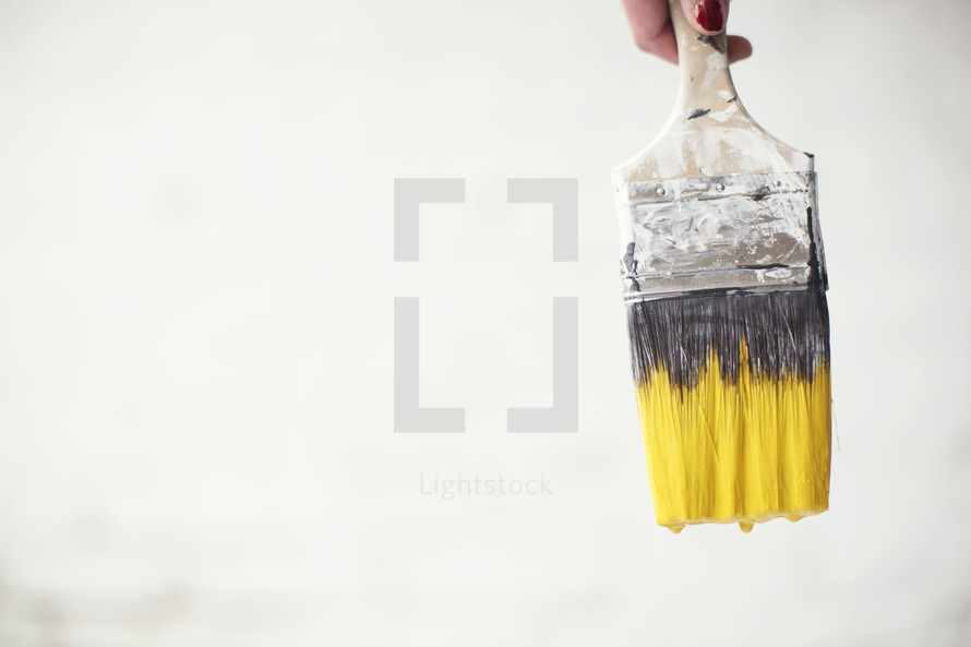 A used paint brush with yellow paint on the bristles.
