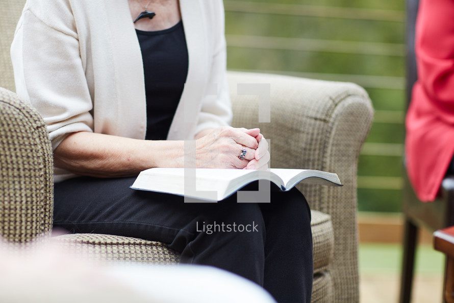 an elderly woman with a Bible in her lap praying 