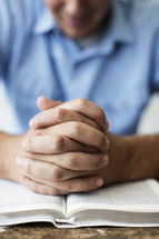 man with praying hands over the pages of a Bible 