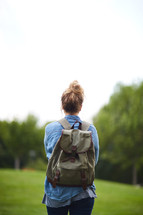 a woman with a backpack standing with her back to the camera 