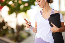 a woman carrying a yoga mat and listening to her iPhone 