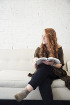 a young woman sitting on a couch reading a Bible 