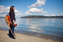 woman standing in front of a lake holding a Bible and a guitar 