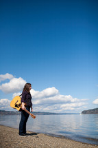 woman holding a guitar in front of a lake