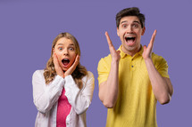 Amazed happy couple expresses WOW. Impressed man woman. Great, unbelievable news, trying to get attention. Concept of sales, profitable offer. Excited friends on violet background. High quality 