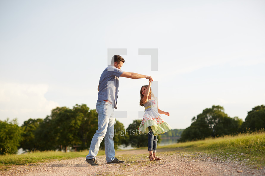 a father dancing with his daughter on a dirt road 