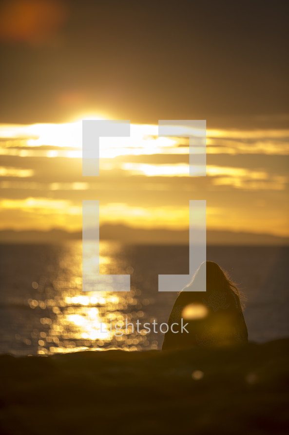 woman sitting on a beach at sunset 