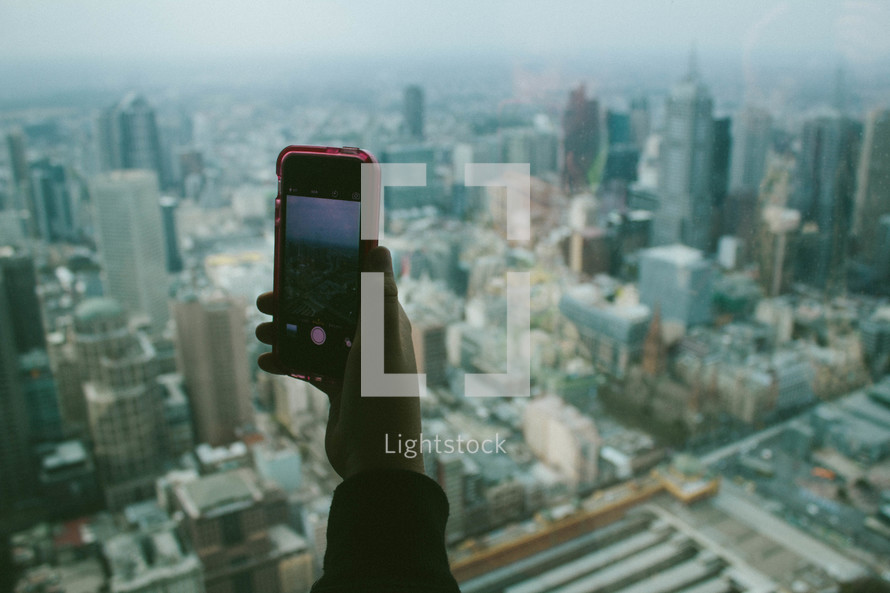 hand holding up a cellphone in front of a cityscape 