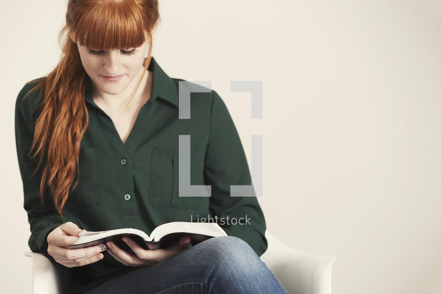 Teen girl sitting in a chair reading the Bible.