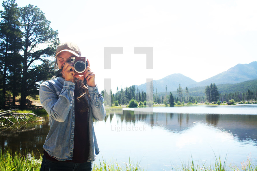 a woman with a camera standing in front of a lake 
