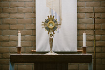 Table with a monstrance and candles in front of a brick wall.