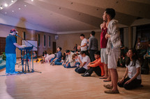 teens sitting on the floor praying during a worship service 