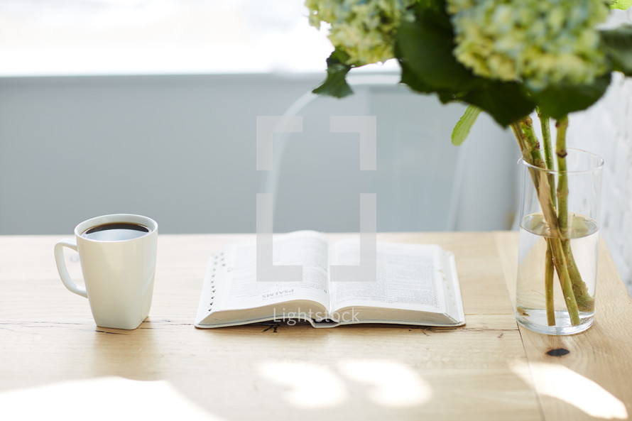 hydrangeas in a vase, coffee cup, and open Bible on a table 