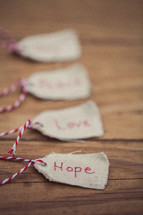 Christmas gift tags lined up on a wood grain background, with the word "Hope" on the first one in line.