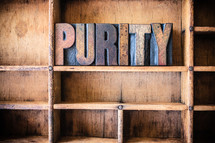 Wooden letters spelling "purity" on a wooden bookshelf.