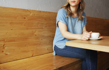a woman with a coffee cup sitting in a booth 