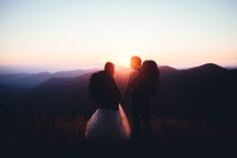 a bride and groom on a mountaintop at sunset 
