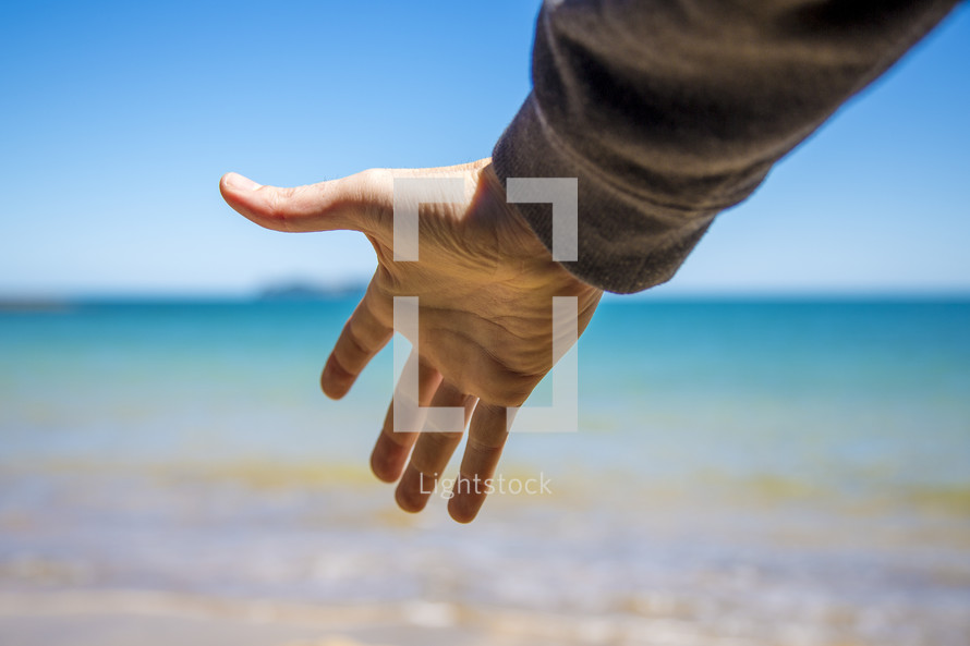 reaching hand towards the ocean 