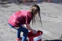 a child wetting a sponge in a bucket for a car wash 