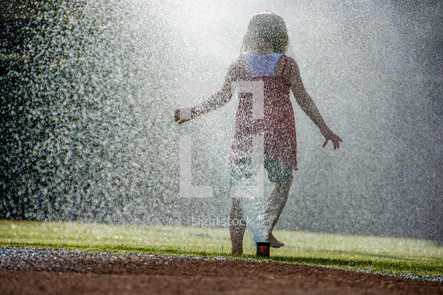 Girl playing and splahing in water sprinklers.