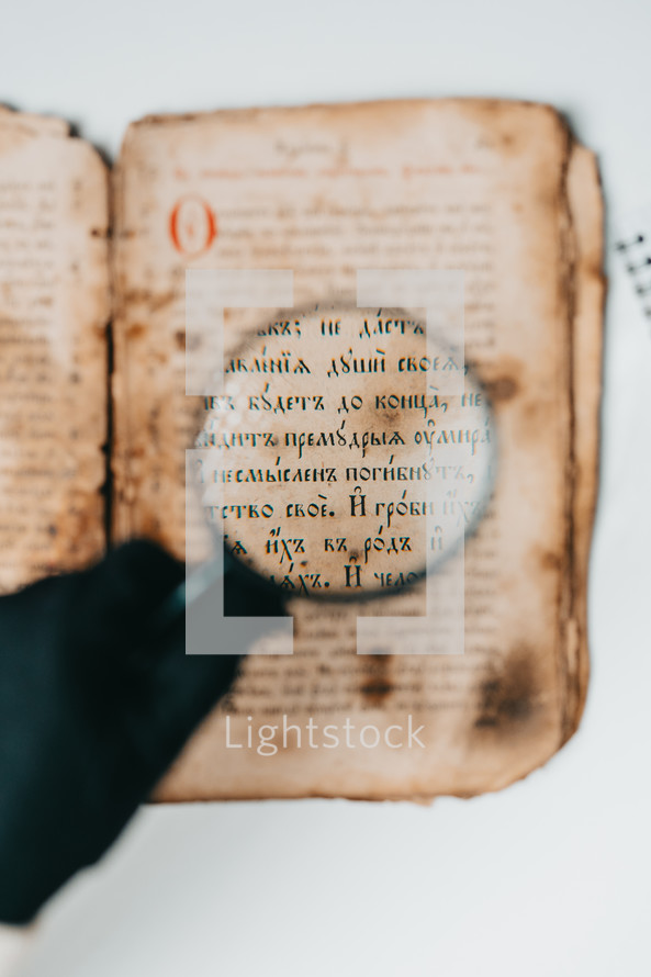 Historian scientist in gloves reading antique book with magnifying glass. Translation of religious literature. Manuscript with ancient writings. Treasures of the past. Museum piece.