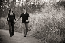 man and pregnant woman holding hands walking on a trail 