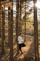 woman leaning against a tree with her hands on her pregnant belly
