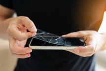 Process unrecognisable repairman is removing broken and old tempered glass screen protector from smartphone, close up view. Services for gluing and replacement of damaged protective glass