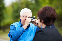 elderly couple sitting on a park bench taking pictures with a camera 