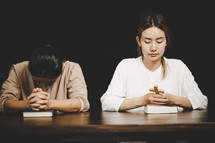 Two Asian women praying together with a cross and Bibles