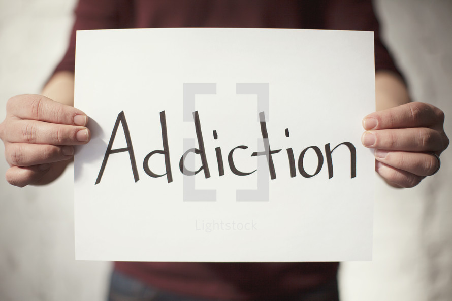 man holding a piece of paper with the word Addiction on it