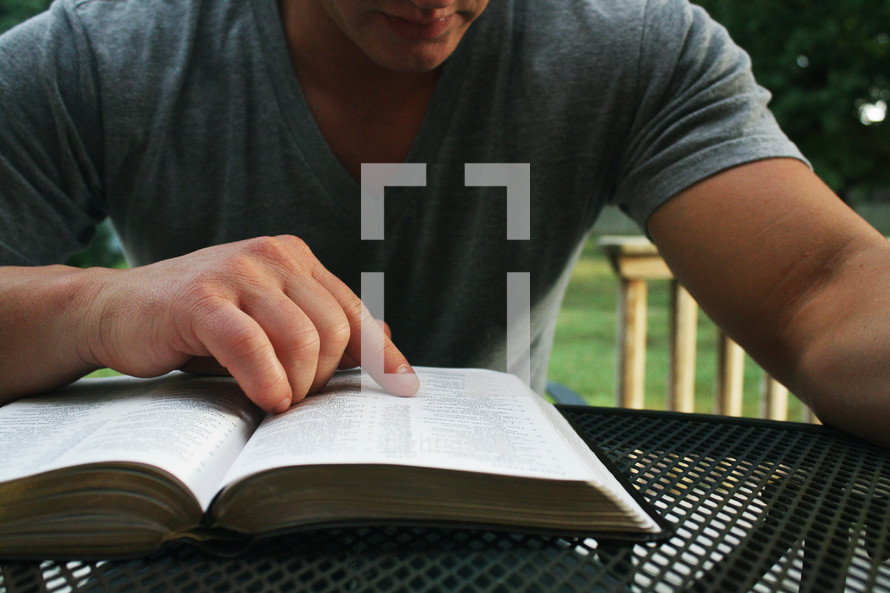 a man reading a Bible at a table outdoors 