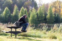 man sitting on a picnic table by a river 