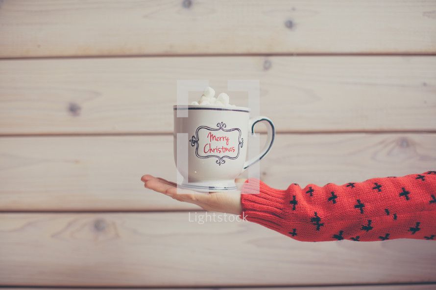 woman holding out a Merry Christmas coffee cup 
