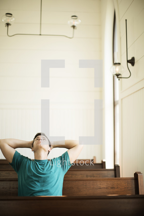 Man looking up and leaning back while praying in a church pew.