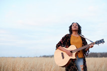 a woman standing in a field with a guitar