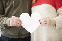 Man and woman standing together holding a white paper heart.